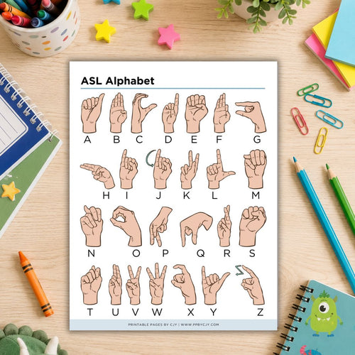 An ASL alphabet printable sheet showing hand gestures for letters A through Z, placed on a desk with notebooks, pencils, paper clips, and star stickers around it.
