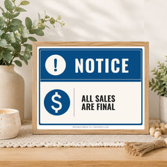 A framed retail notice sign on a wooden table with plants and decor. The sign has a blue and white design with the text 'NOTICE' and 'ALL SALES ARE FINAL'.