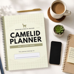 A spiral-bound Camelid Planner notebook shown in a styled flat-lay on a white surface, surrounded by a cup of coffee, a pen, a small succulent, a smartphone, and another notebook.