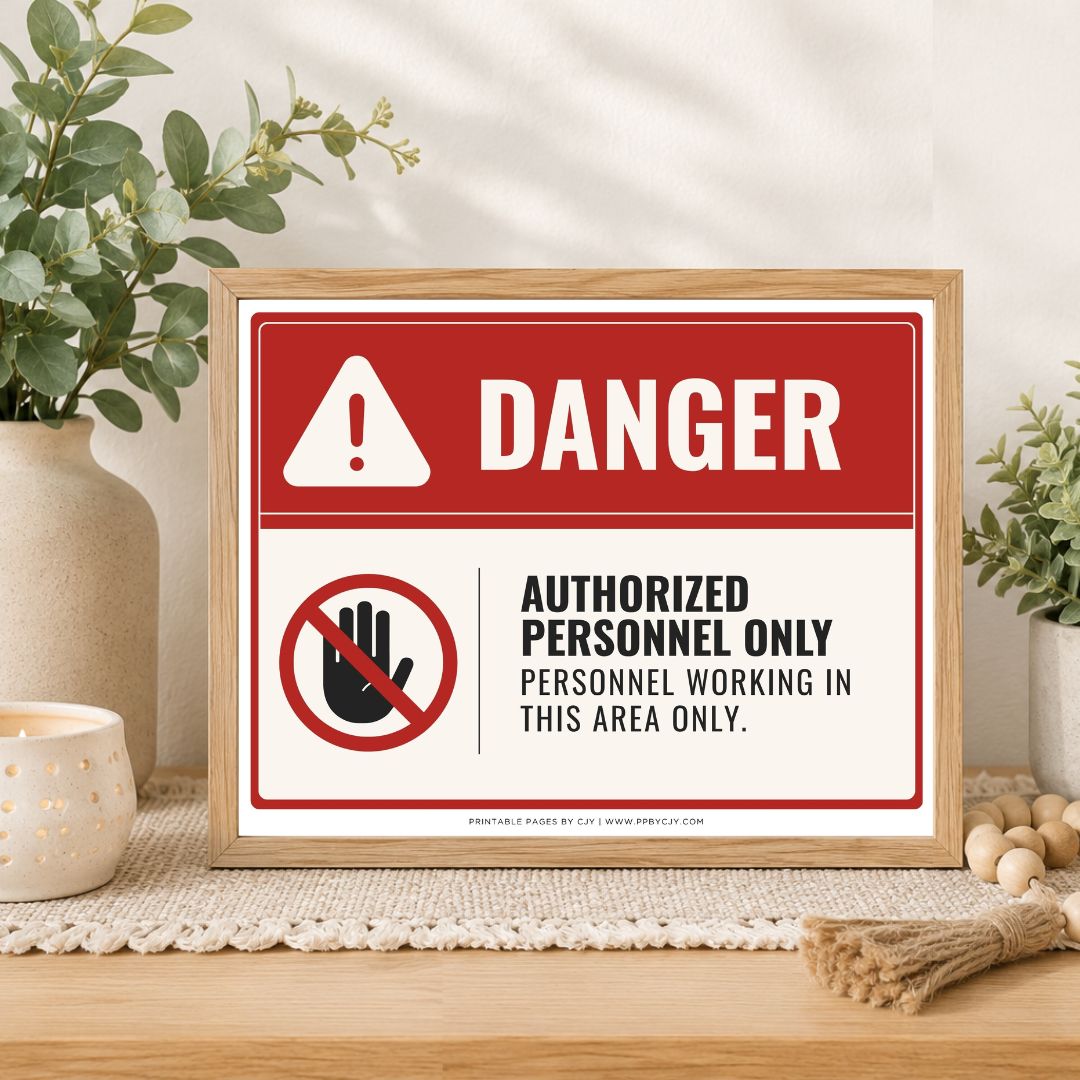 A framed warning sign with a red and white background, featuring the word 'DANGER' and a crossed-out hand icon with the text 'AUTHORIZED PERSONNEL ONLY PERSONNEL WORKING IN THIS AREA ONLY.' The sign is displayed on a wooden surface with decorative plants and candles in the background.