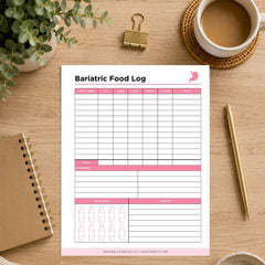 A printable bariatric food log sheet displayed on a wooden desk with a coffee cup, plant, binder clip, notebook, and pen around it. The sheet has pink headers and a grid for tracking food intake by meal and time.