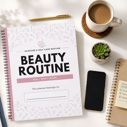 A spiral-bound beauty routine planner lies on a white desk surrounded by a cup of coffee, a small succulent, a smartphone, and other notebooks. The planner cover is white with black text reading 'BEAUTY ROUTINE' and a pink accent bar, decorated with faint cosmetic icons.