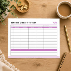 A printed Behcet's Disease Tracker sheet laid on a wooden desk with a coffee cup, plant, binder clips, pen, and notebook around it. The sheet has a white background with purple header accents and table lines.