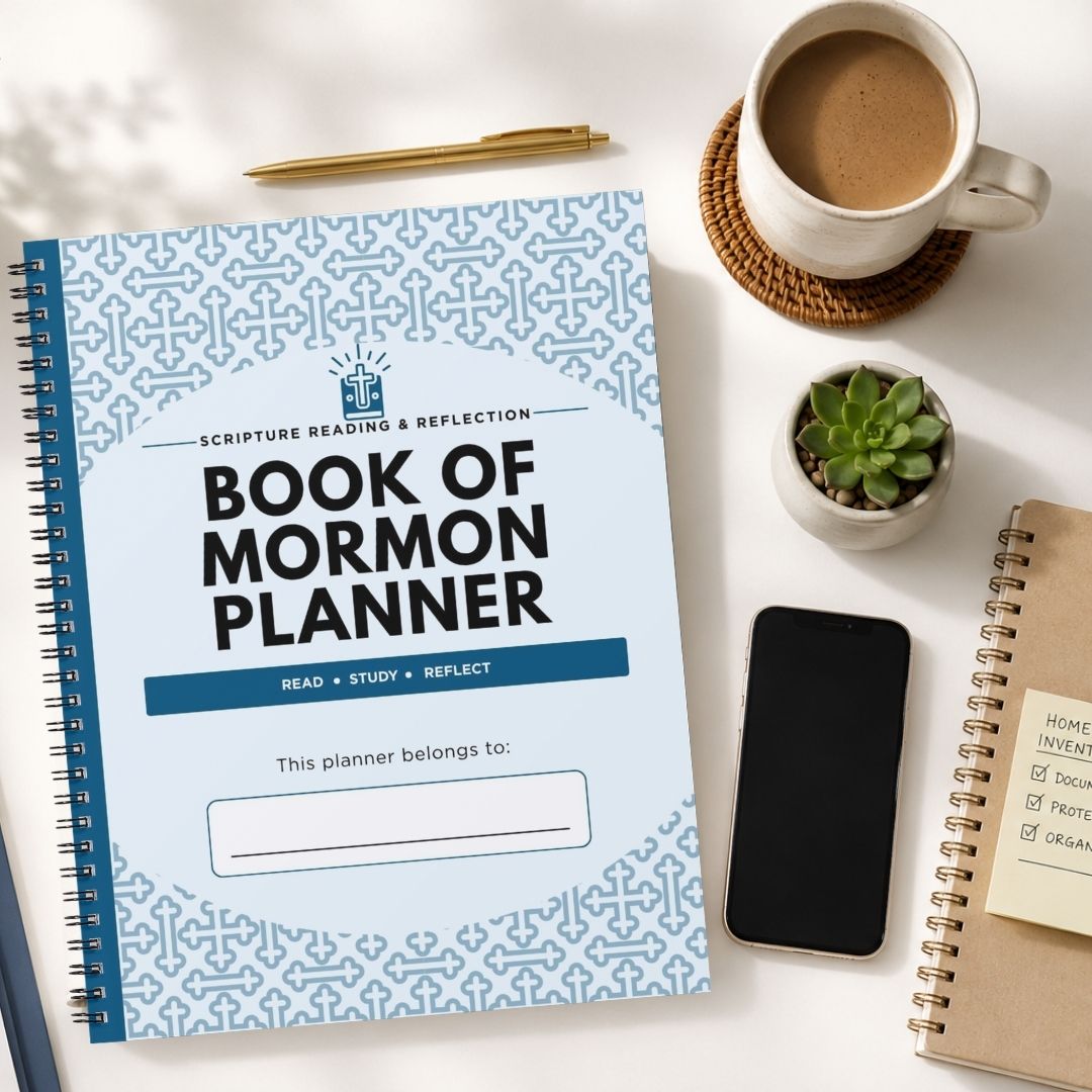 A spiral-bound Book of Mormon Planner with a light blue patterned cover is shown in a styled flat-lay on a white surface, surrounded by a coffee cup, a pen, a small succulent, a smartphone, and another notebook.