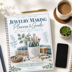 A spiral-bound journal titled 'Jewelry Making Planner & Guide' lies on a white surface, surrounded by a cup of coffee, a pen, a small succulent, a smartphone, and other crafting props. The cover features a styled illustration with beads, wire, pliers, and greenery.
