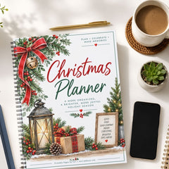 A spiral-bound Christmas Planner laid on a white desk, surrounded by a coffee cup, a small succulent, a smartphone, and another notebook. The planner cover features festive illustrations including a red bow, green pine branches, a lantern, wrapped gifts, and the title 'Christmas Planner' in red and green text.