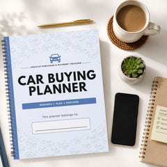 A spiral-bound 'Car Buying Planner' notebook is displayed in a styled flat-lay arrangement on a white desk, surrounded by a cup of coffee, a smartphone, a small succulent, and other notebooks.