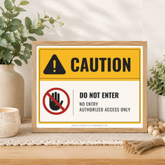 A framed warning sign with a yellow and white background, featuring a caution icon and the text 'CAUTION' and 'DO NOT ENTER / NO ENTRY AUTHORIZED ACCESS ONLY.' The sign is displayed on a tabletop with decorative plants, a candle, and a burlap bundle in a styled interior setting.