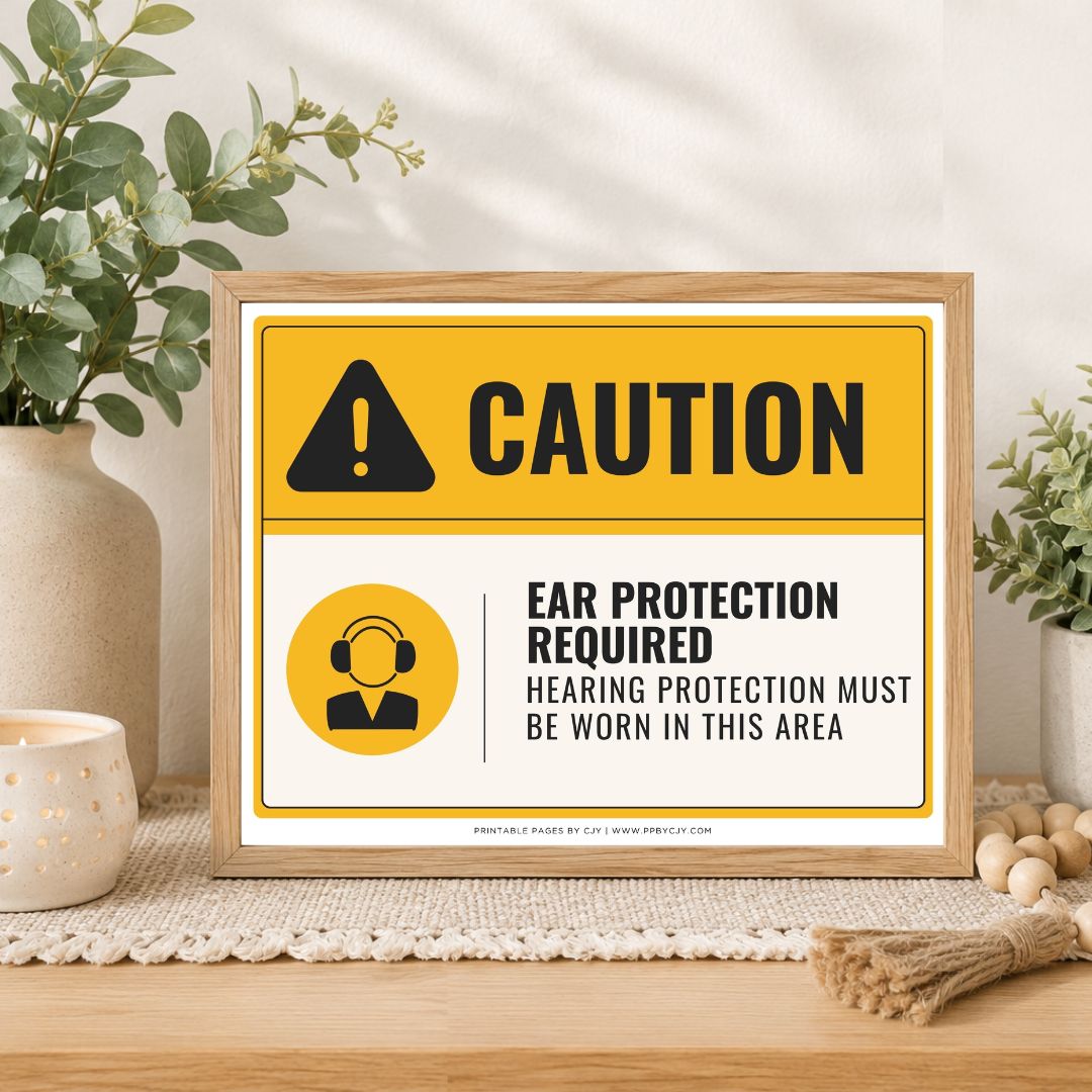 A framed caution sign with a yellow and white background, black text reading 'CAUTION' and 'EAR PROTECTION REQUIRED / HEARING PROTECTION MUST BE WORN IN THIS AREA,' styled on a tabletop with plants and home decor props.