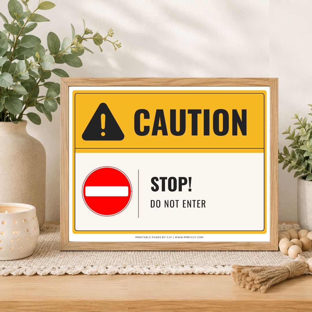 A framed novelty warning sign on a wooden table, styled with plants and home decor. The sign features a yellow and white background with a black caution icon, the word 'CAUTION', a red circle with a white horizontal bar, and the text 'STOP! DO NOT ENTER'.