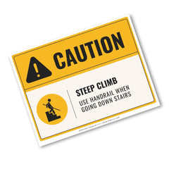 A rectangular caution-style sign with a yellow header, black warning icon, and text reading 'CAUTION' and 'STEEP CLIMB USE HANDRAIL WHEN GOING DOWN STAIRS' on a white background.