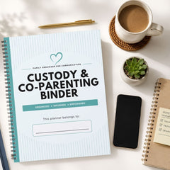 A spiral-bound planner titled 'CUSTODY & CO-PARENTING BINDER' laid on a white desk, surrounded by a coffee cup, pen, small succulent, smartphone, and another notebook.