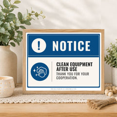 A framed printed notice sign on a tabletop, styled with plants, a candle, and decorative beads. The sign reads “NOTICE” and “CLEAN EQUIPMENT AFTER USE THANK YOU FOR YOUR COOPERATION.
