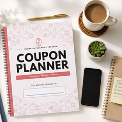 A spiral-bound Coupon Planner notebook lies on a white desk surrounded by a cup of coffee, a small potted succulent, a smartphone, and another notebook. The planner cover is white with pink budget and finance icons, large black 'COUPON PLANNER' text, and a coral-red horizontal bar.