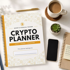 A spiral-bound Crypto Planner notebook is shown in a styled flat-lay arrangement on a white surface, alongside a cup of coffee, a small succulent, a smartphone, and another notebook.