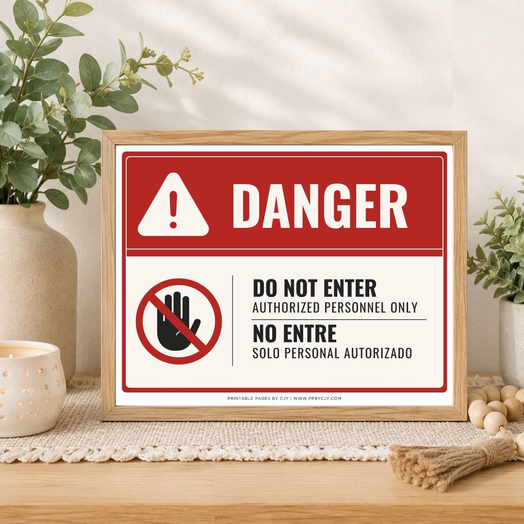A framed warning sign with a red and white background, featuring the word DANGER, a prohibition symbol, and the text 'DO NOT ENTER AUTHORIZED PERSONNEL ONLY' in both English and Spanish, styled on a wooden table with plants and home decor.