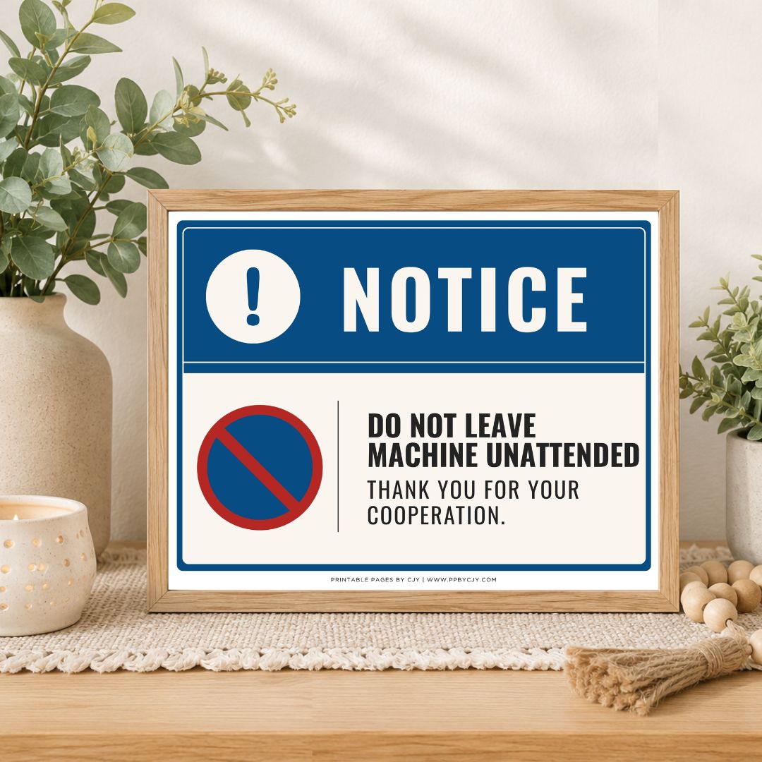A framed warning sign with a blue and white background sits on a wooden table in a styled home setting. The sign reads 'NOTICE' and 'DO NOT LEAVE MACHINE UNATTENDED' with a red and blue no-entry symbol.