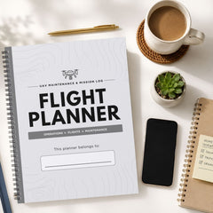 A spiral-bound UAV drone flight misson planner is shown in a styled flat-lay arrangement on a white surface, surrounded by a cup of coffee, a pen, a small succulent, a smartphone, and another notebook.