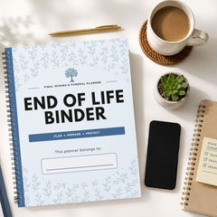 A spiral-bound 'End of Life Binder' planner is displayed in a styled flat-lay arrangement on a white desk alongside a cup of coffee, a smartphone, a small succulent, and other notebooks.