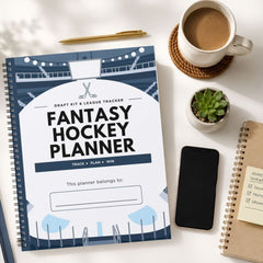 A spiral-bound fantasy hockey planner lies on a white desk surrounded by a coffee cup, a pen, a small succulent, a smartphone, and another notebook.