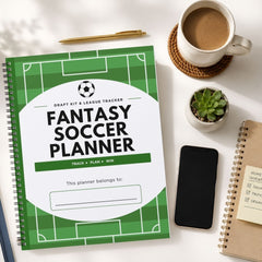 A spiral-bound Fantasy Soccer Planner notebook is shown in a styled flat-lay on a white desk, surrounded by a coffee cup, a pen, a small succulent, a smartphone, and another notebook.