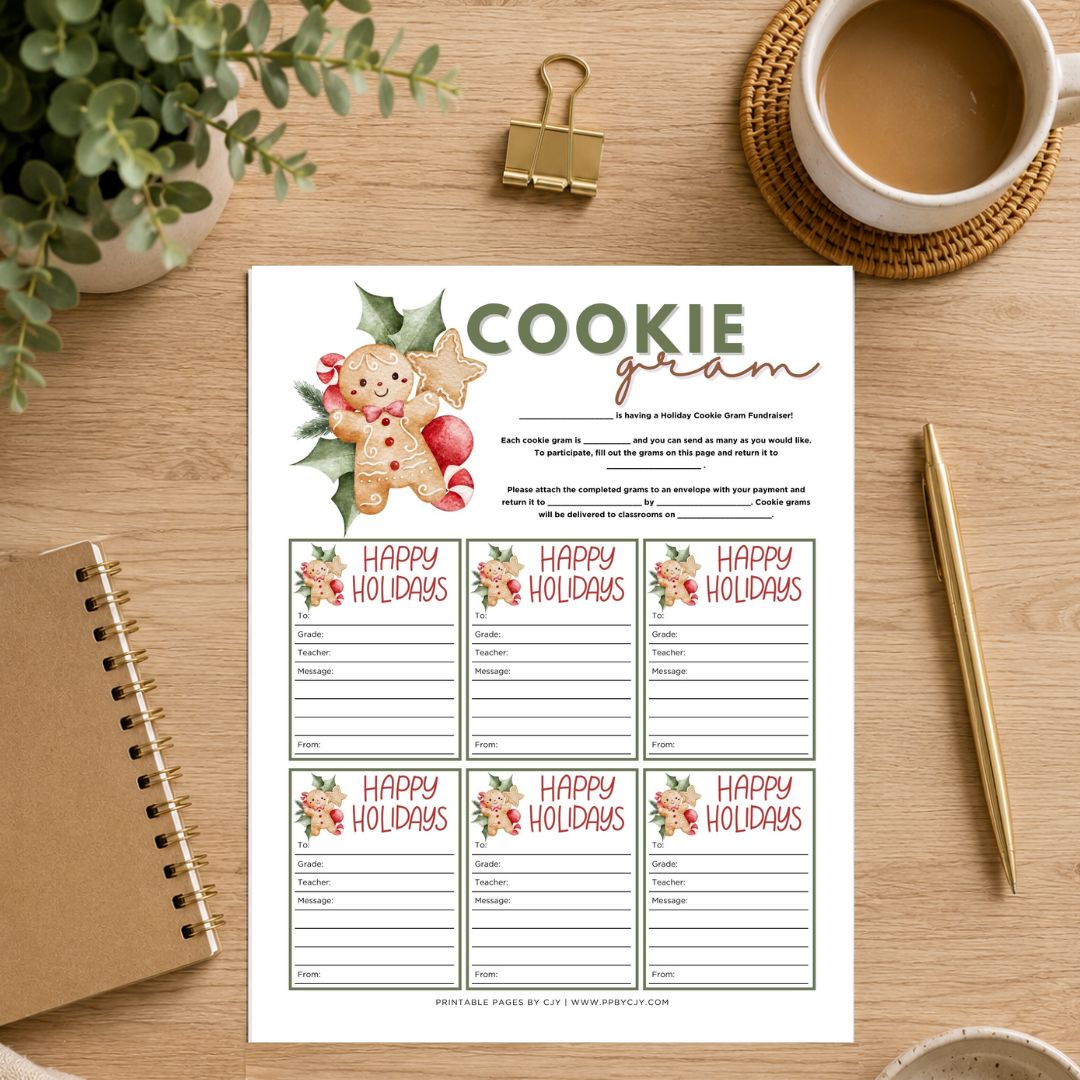 A printable holiday cookie game sheet displayed on a wooden desk with a coffee cup, notebook, pen, and plant. The white sheet features a gingerbread man illustration and the title 'COOKIE gram' at the top, with six 'HAPPY HOLIDAYS' activity boxes below.