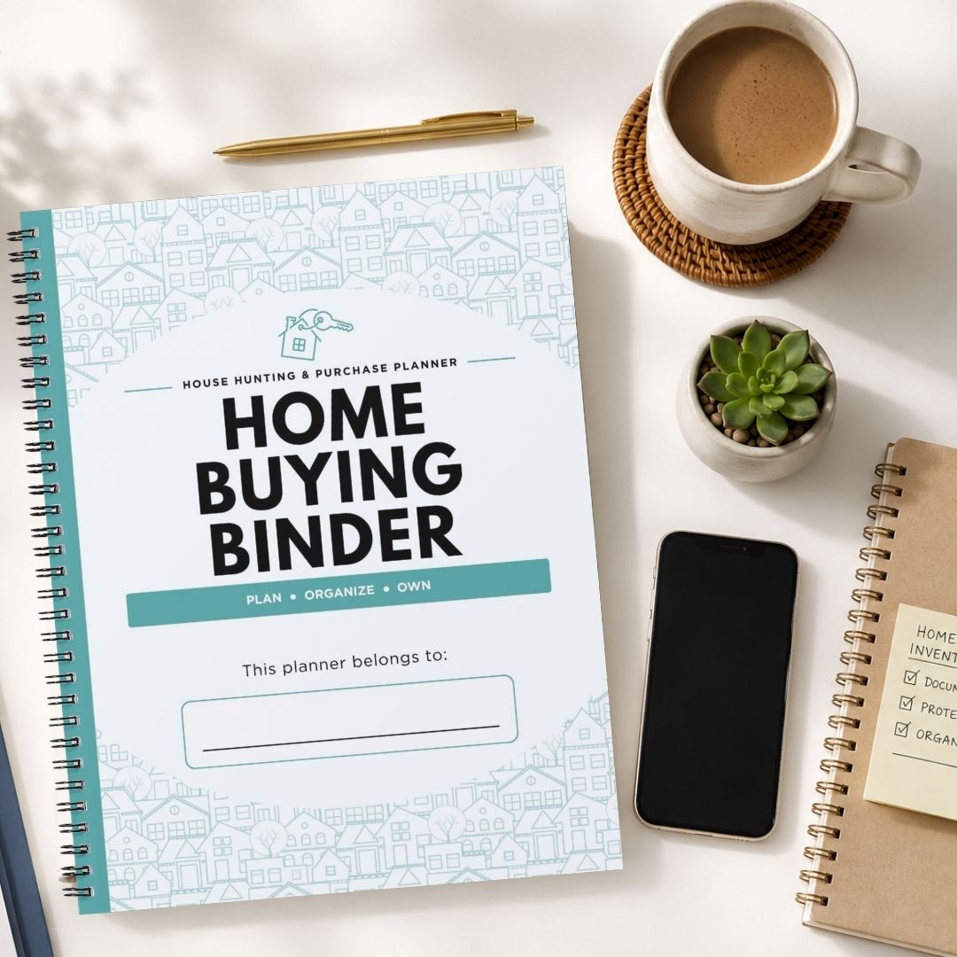 A spiral-bound 'Home Buying Binder' planner is displayed in a styled flat-lay arrangement on a white surface, surrounded by a coffee cup, a pen, a small succulent, a smartphone, and another notebook.