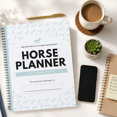 A spiral-bound horse planner organizer with a white cover and light blue horse silhouettes, styled in a flat lay with a coffee cup, pen, succulent, smartphone, and another notebook on a white surface.
