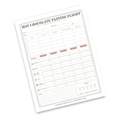 A printable 'Hot Chocolate Tasting Flight' log sheet shown at an angle on a white background. The sheet features columns for date, time, temperature, chocolate type, notes, and a weekly rating grid with emoji icons.