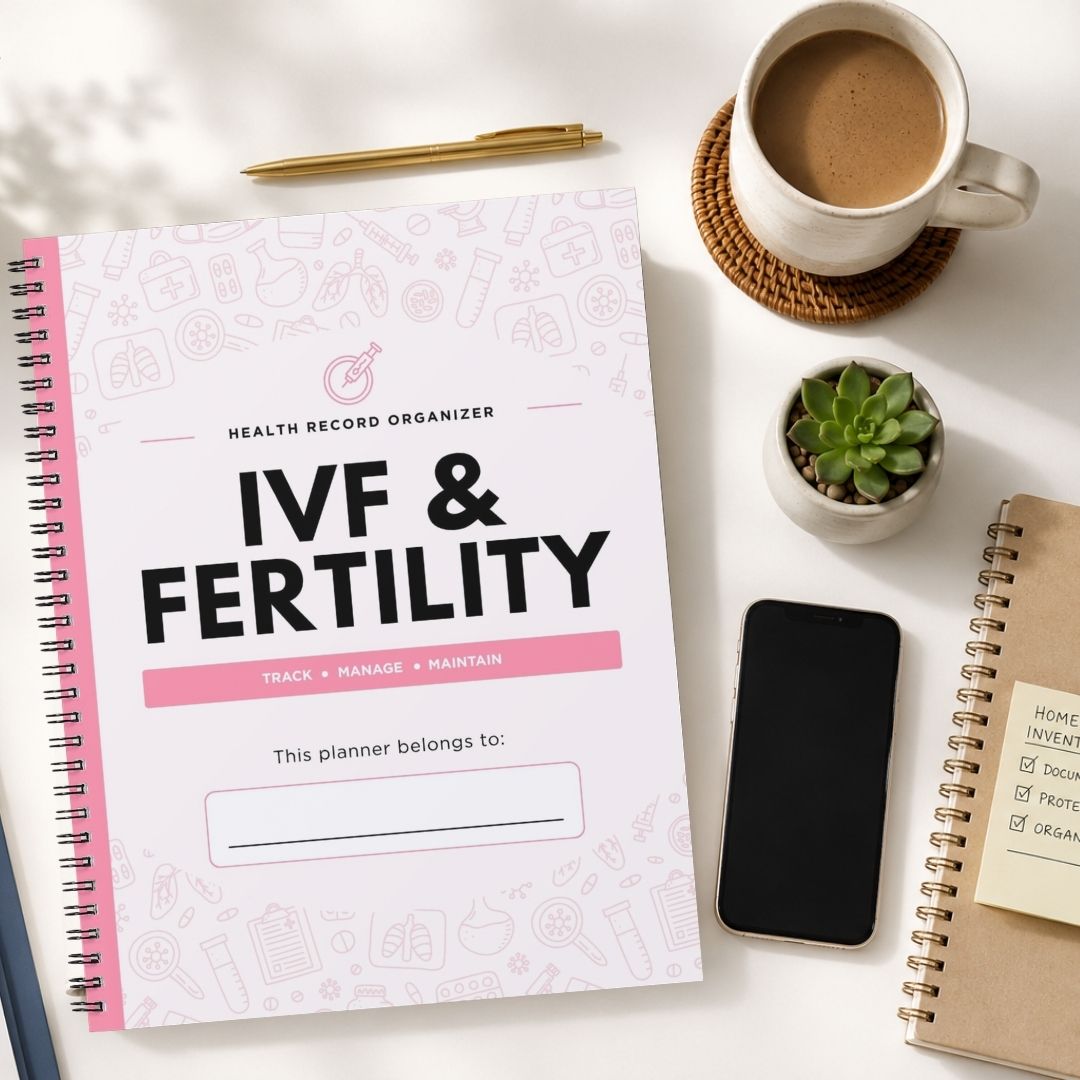 A spiral-bound health record organizer titled 'IVF & Fertility' lies on a white desk, surrounded by a coffee cup, pen, small succulent, smartphone, and another notebook.