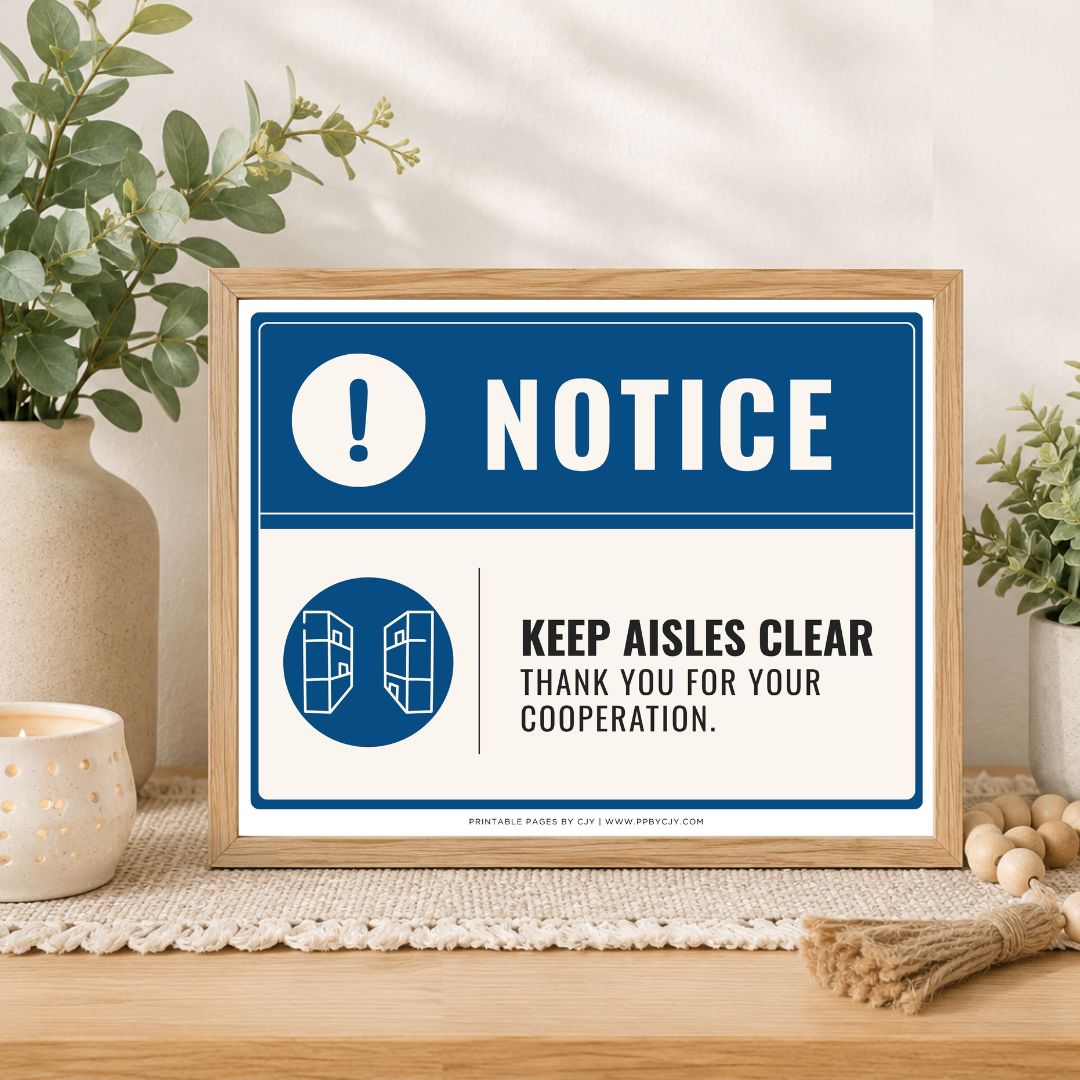 A framed printed notice sign on a tabletop, styled with plants, a candle, and decorative beads. The sign has a blue header with a white exclamation mark and the word NOTICE, and a white lower section that reads 'KEEP AISLES CLEAR THANK YOU FOR YOUR COOPERATION.