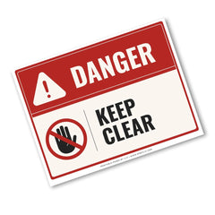 A rectangular warning sign with a red header reading DANGER and a white lower section that says KEEP CLEAR, plus a hand icon with a red slash. The sign is shown at an angle on a light gray background.