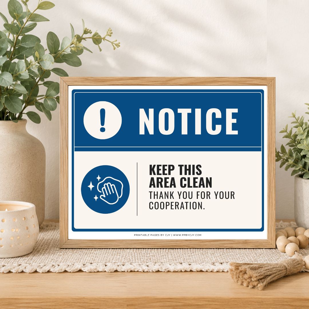 A framed printed notice sign on a wooden table, styled with plants, a candle, and decorative beads. The sign has a blue and white design with the word 'NOTICE' and a hand-cleaning icon, reading 'KEEP THIS AREA CLEAN THANK YOU FOR YOUR COOPERATION.