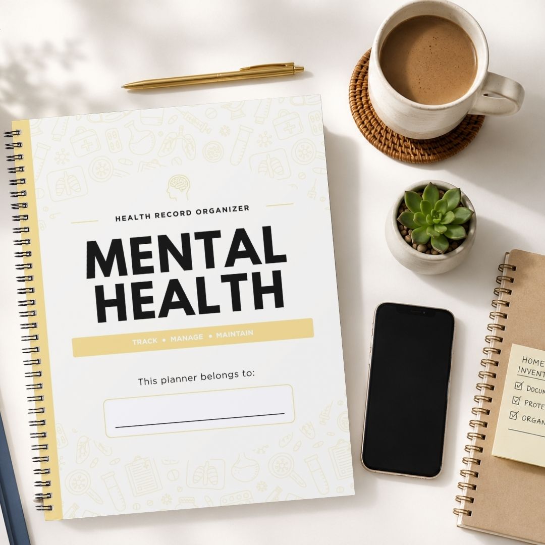 A spiral-bound health record organizer titled 'MENTAL HEALTH' lies on a white desk, surrounded by a coffee cup, pen, small succulent, smartphone, and another notebook.