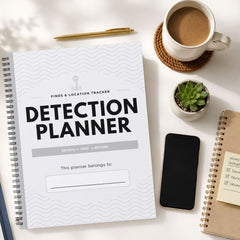 A spiral-bound notebook titled 'DETECTION PLANNER' laid on a white desk, surrounded by a coffee cup, pen, small succulent, smartphone, and another notebook.