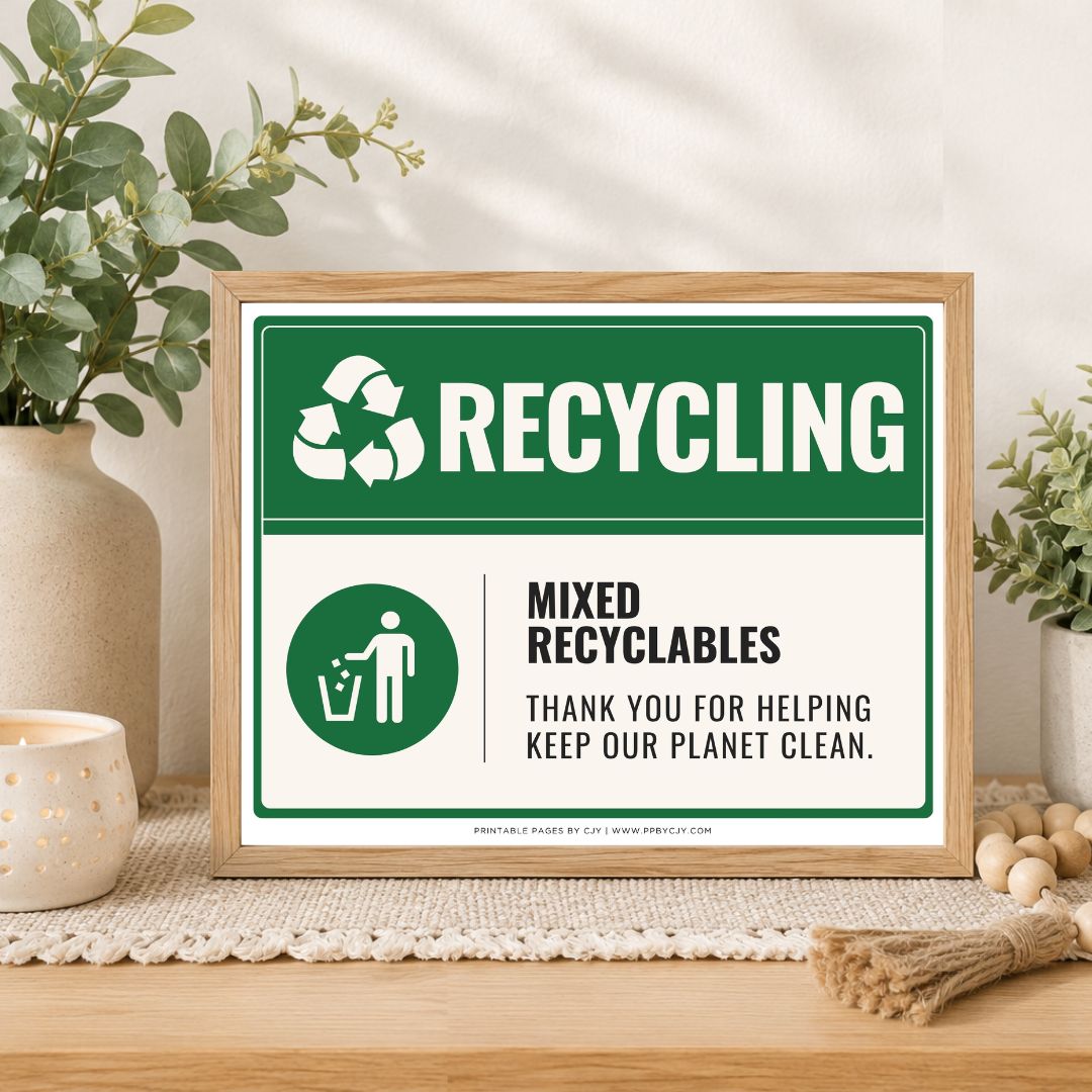 A framed recycling sign displayed on a wooden table in a styled home setting with plants and a candle. The sign features a green and white design with the text 'RECYCLING' and 'MIXED RECYCABLES THANK YOU FOR HELPING KEEP OUR PLANET CLEAN.