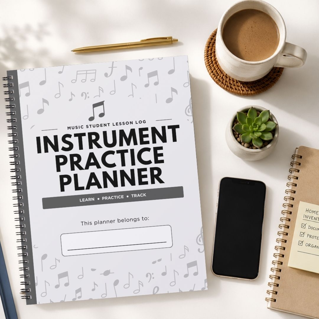 A spiral-bound 'Instrument Practice Planner' with a white cover decorated with gray musical notes, styled in a flat-lay on a white desk alongside a cup of coffee, a pen, a small succulent, a smartphone, and another notebook.