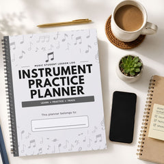 A spiral-bound 'Instrument Practice Planner' with a white cover decorated with gray musical notes, styled in a flat-lay on a white desk alongside a cup of coffee, a pen, a small succulent, a smartphone, and another notebook.