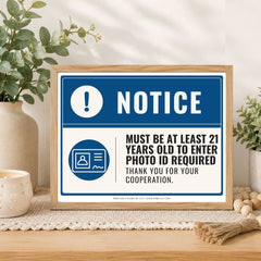 A framed novelty sign with a blue and white design sits on a wooden table in a styled home setting with plants and decorative items.
