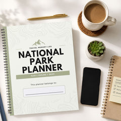A spiral-bound National Park Planner labeled 'Travel Memory Log' is shown in a styled flat-lay with a coffee cup, pen, phone, small plant, and another notebook on a light surface.