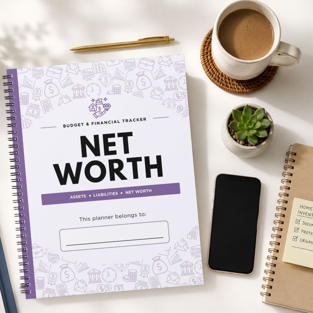 A spiral-bound Net Worth Budget & Financial Tracker planner is shown in a styled flat-lay arrangement on a white surface, surrounded by a cup of coffee, a pen, a small succulent, a smartphone, and another notebook.