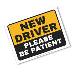 A rectangular warning-style sign with a yellow top half and black bottom half, reading “NEW DRIVER PLEASE BE PATIENT” in bold text, shown on a plain white background.