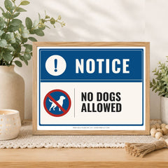 A framed 'No Dogs Allowed' sign displayed on a wooden table in a styled home setting with plants and decorative items.