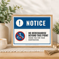 A framed novelty warning sign displayed on a wooden table in a styled home setting. The sign features a blue and white design with the text 'NOTICE' and 'NO MERCHANDISE BEYOND THIS POINT THANK YOU FOR YOUR COOPERATION.