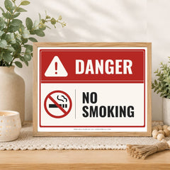 A framed 'DANGER NO SMOKING' sign with a red and white design, displayed on a wooden table in a styled home setting with plants and a candle.