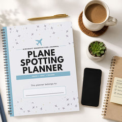 A spiral-bound 'Plane Spotting Planner' lies on a white desk surrounded by lifestyle props including a cup of coffee, a smartphone, a small succulent, and another notebook.