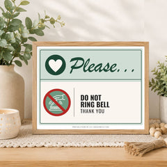 A framed printed sign on a wooden table in a styled interior setting. The sign reads 'Please.