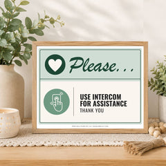A framed printed sign on a wooden table in a styled interior setting. The sign reads 'Please.