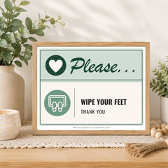 A framed novelty sign on a wooden table in a styled home setting, featuring a light wood frame, a sage green and white background, and the text 'Please.