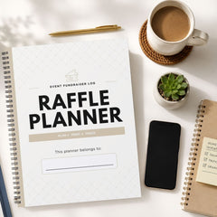 A white spiral-bound 'Raffle Planner' with black text and a subtle diamond pattern, styled in a flat-lay arrangement on a white desk alongside a coffee cup, a pen, a smartphone, a small succulent, and another notebook.